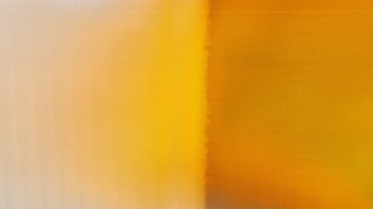 A soft, heavily blurred abstract in warm tones, shading from pale cream on the left through golden yellow to deep amber and orange on the right, with a faint vertical seam down the middle.